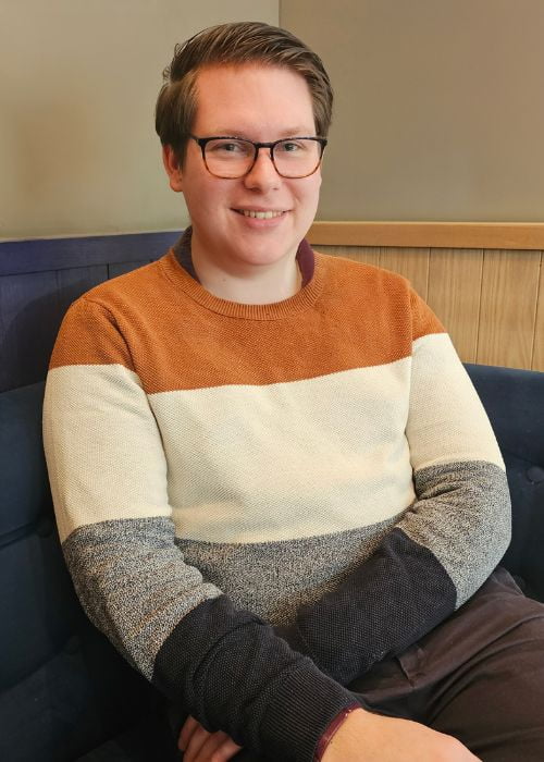 Young man with brown hair, looking at the camera smiling with his arms crossed.