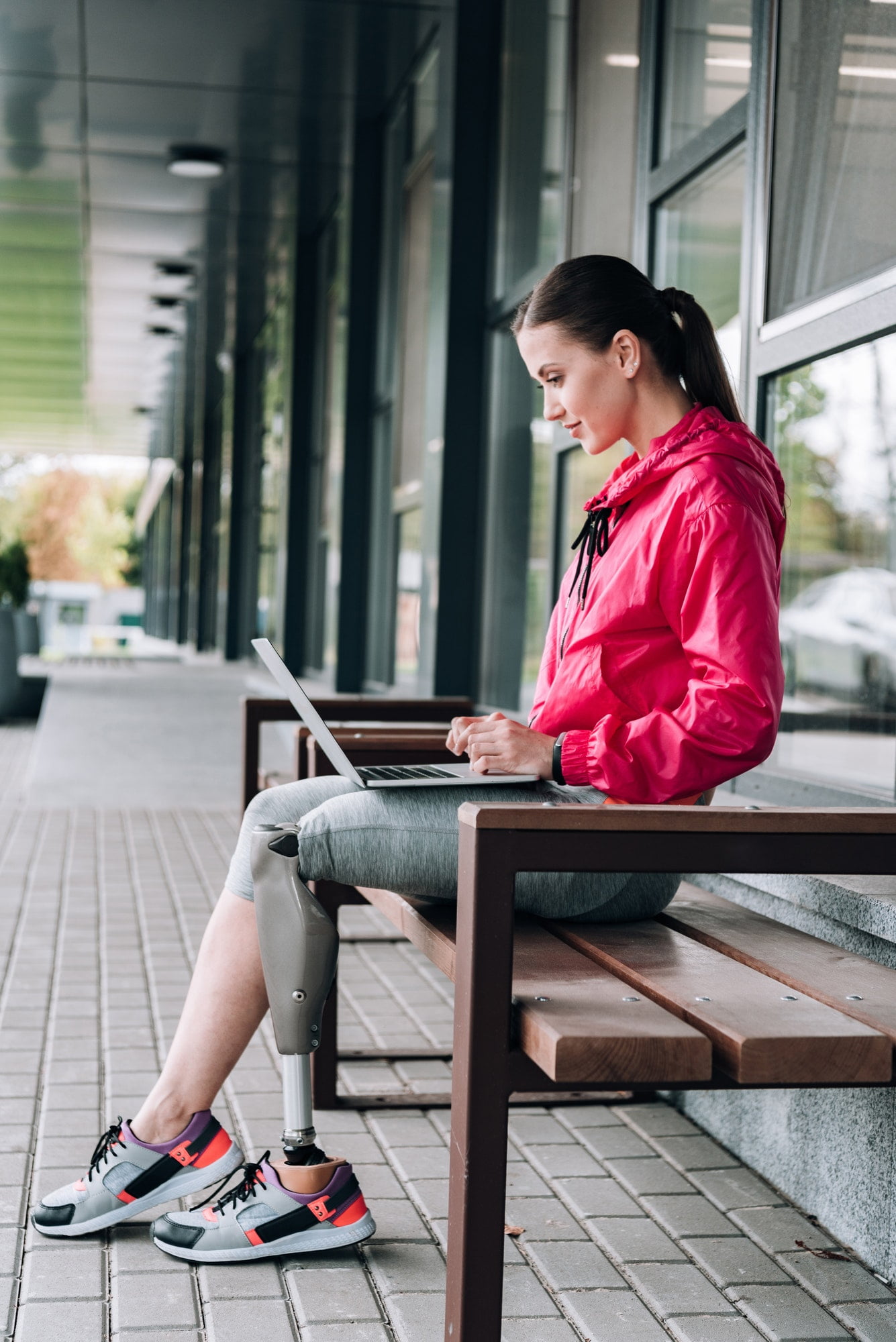 Side view of disabled woman sitting on bench and using laptop