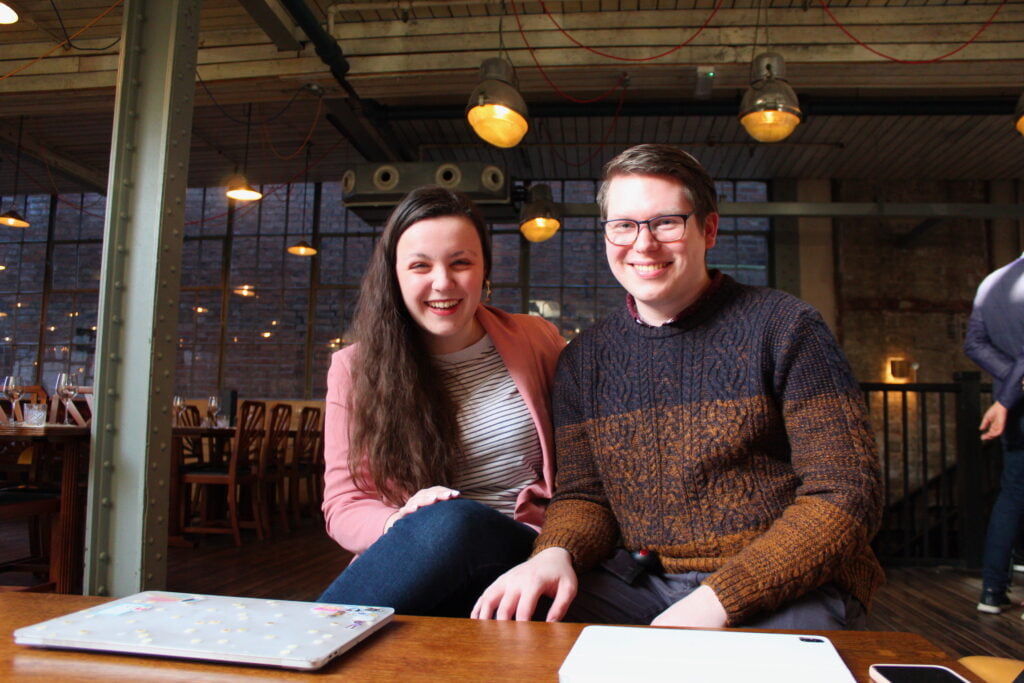 Man and Woman sitting in a coffee shop with laptops smiling