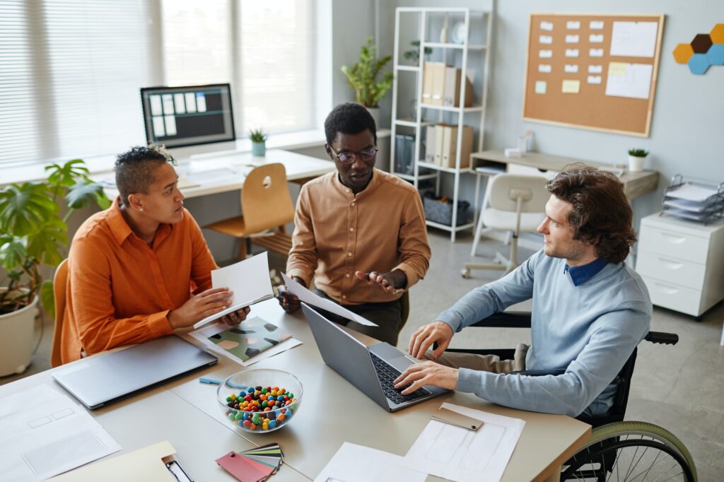 Three team members sat around a desk with laptops talking