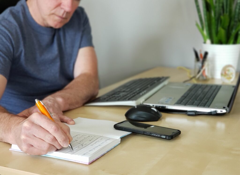 Man is writing in the journal working from home