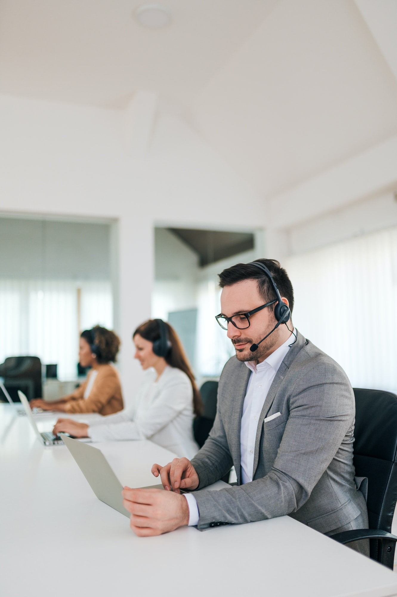 People wearing headsets in an office, working on laptops