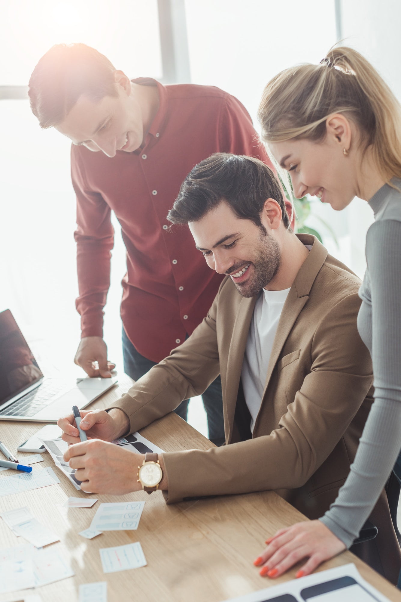 Three businesspeople laughing and talking while looking at paperwork in office