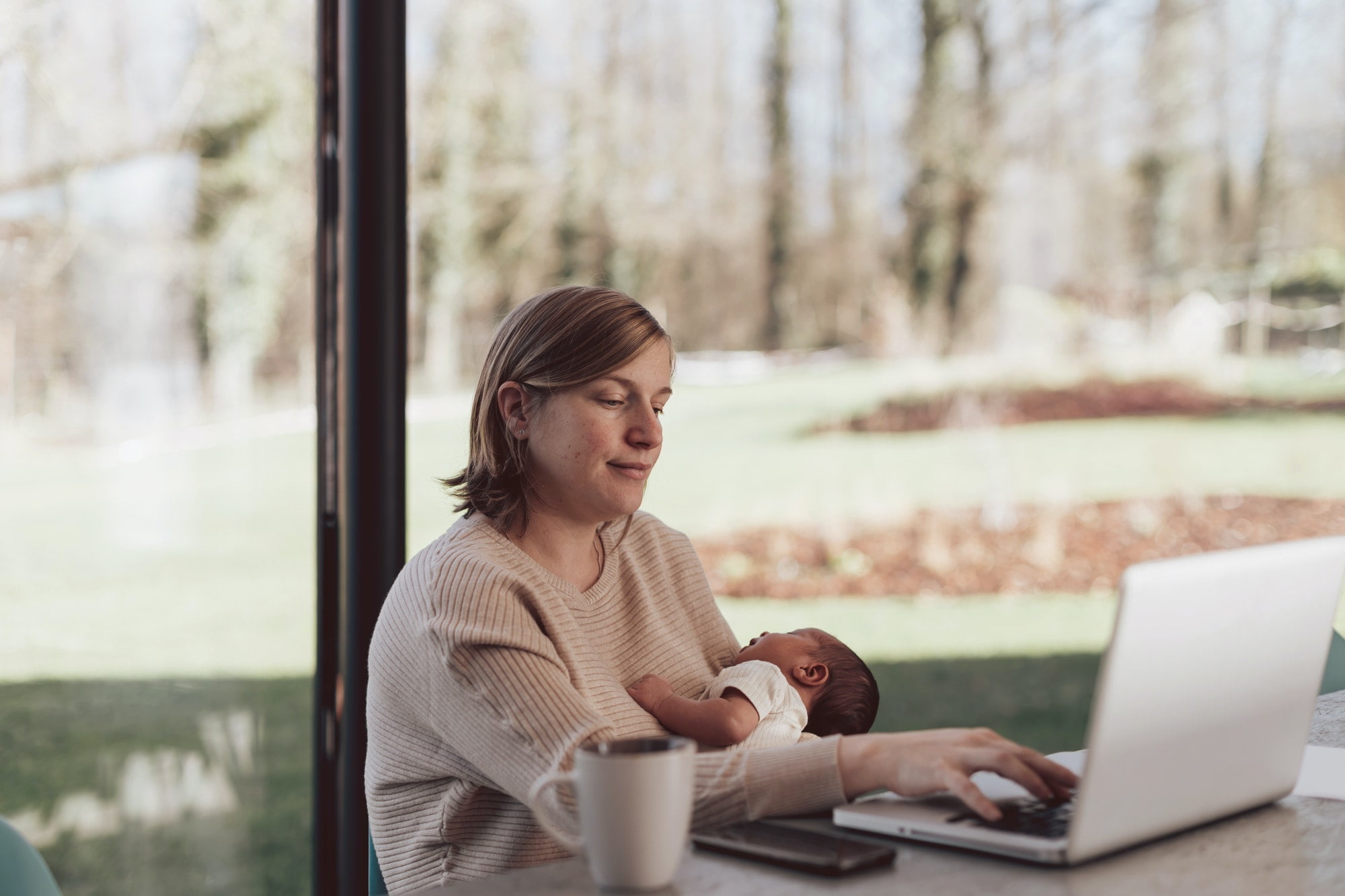 New Mum working on laptop while holding baby