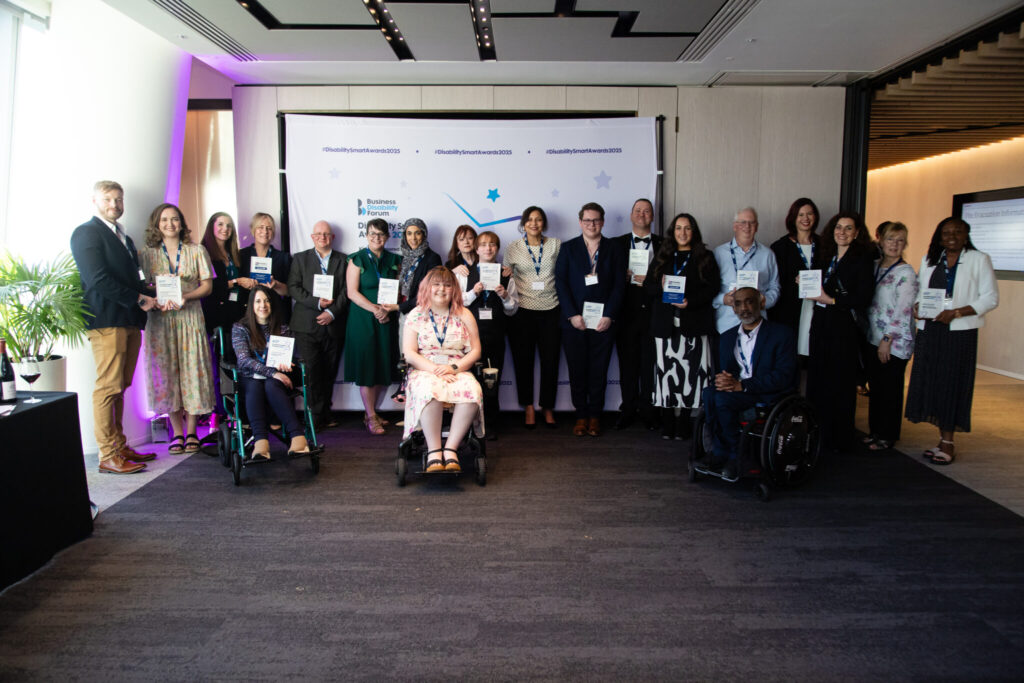 A group photo of the 2025 Disability Smart Award winners standing and seated in front of a branded backdrop displaying the Business Disability Forum logo and the hashtag #DisabilitySmartAwards2025. Twenty-one people are present, holding plaques or smiling proudly. Two individuals are seated in wheelchairs at the front, including a young woman in a floral dress with pink hair and a man in a suit. Another woman is seated in a green wheelchair on the left. The atmosphere is professional and celebratory, with soft purple lighting on the left and natural light coming from the windows.


Inkfire wins Disability Smart Award 2025 